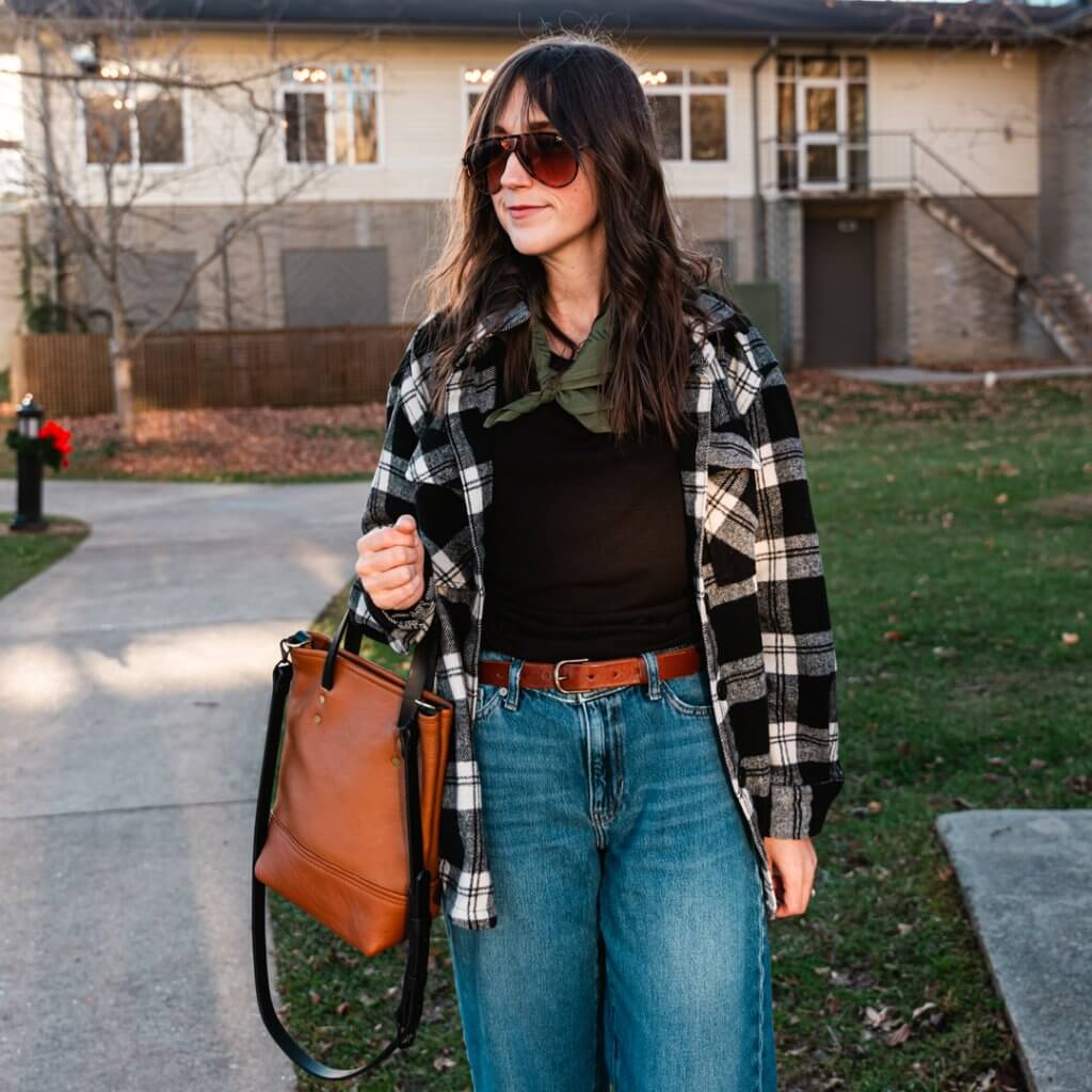 a woman stands with a leather bag and belt on a sidewalk in the park