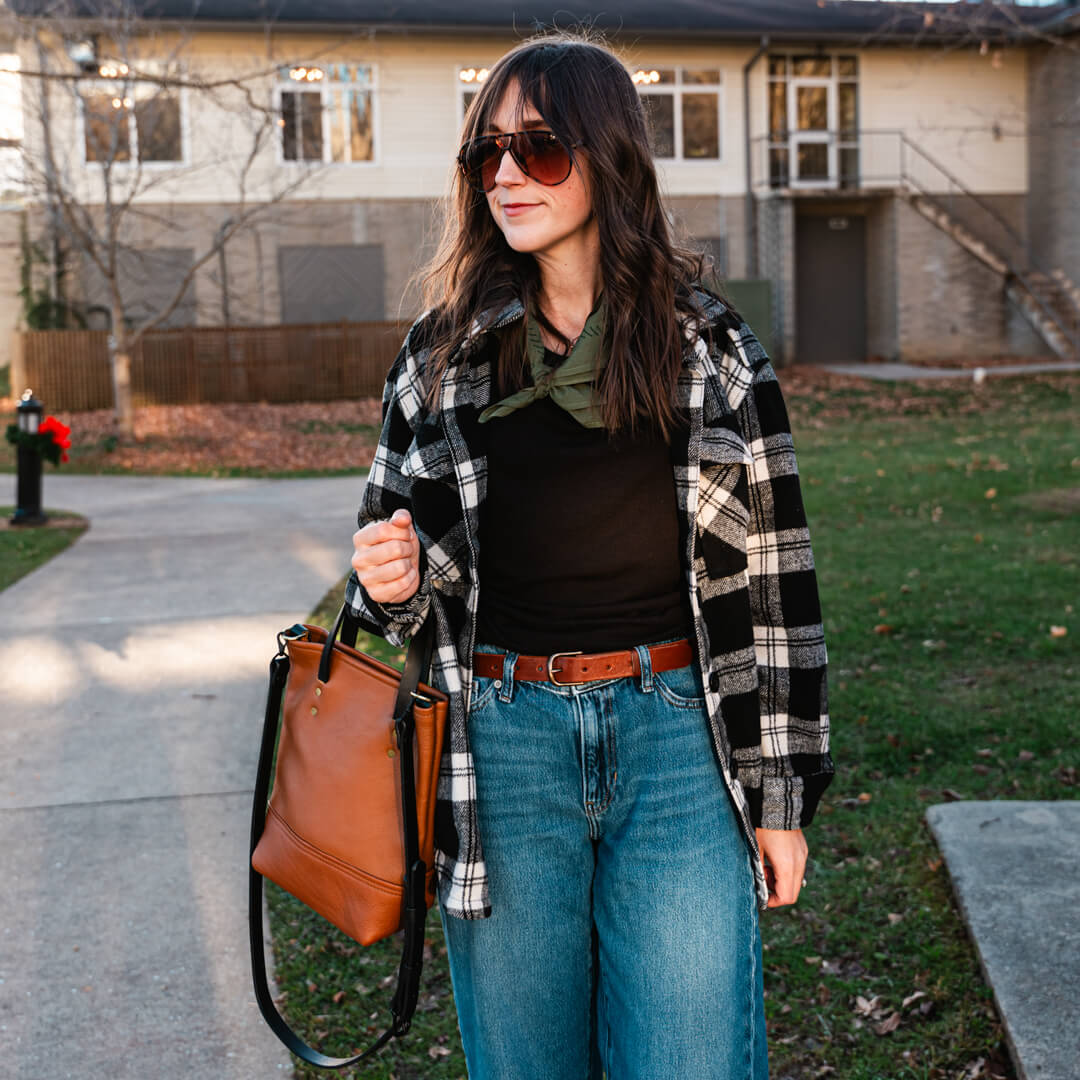 a woman stands with a leather bag and belt on a sidewalk in the park