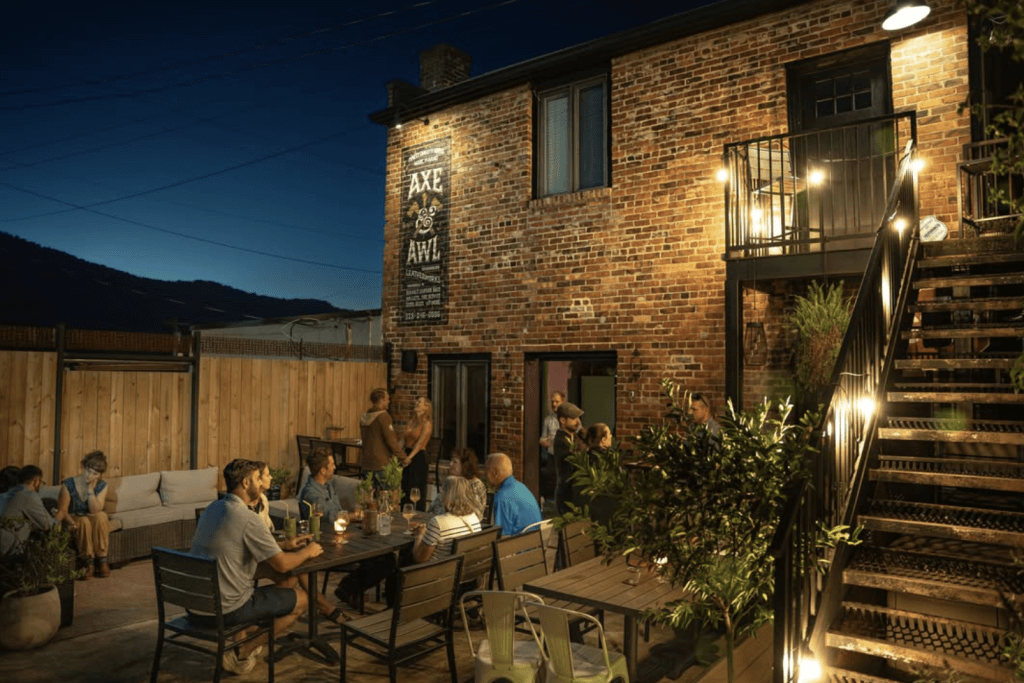 the back patio of axe and awl leather shop when it operates as bevel bar. pictured people drinking at night, with the small business open inside. 