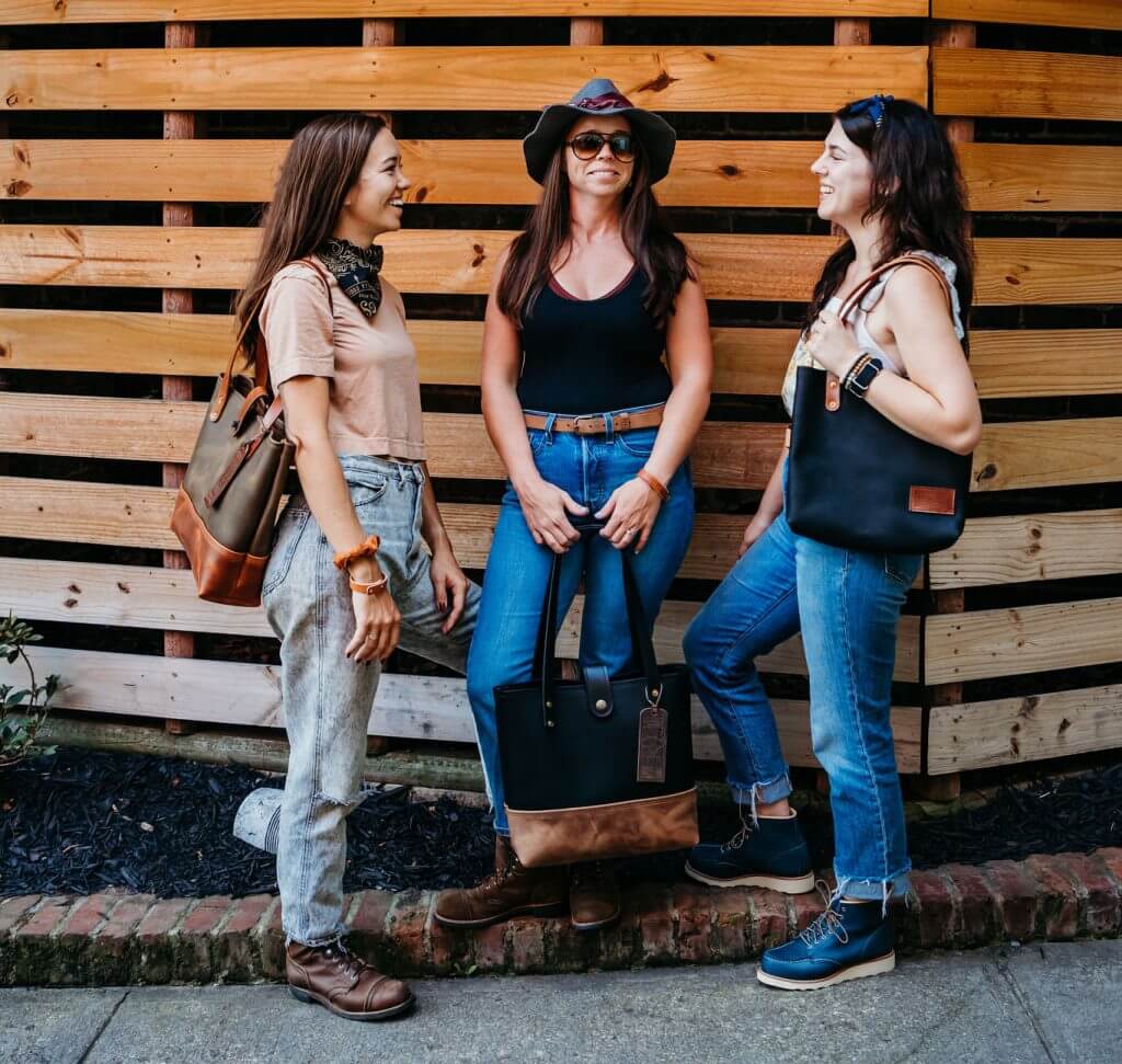 Three women holding axe and awl bags talking on a street corner in waynesville, north carolina. 