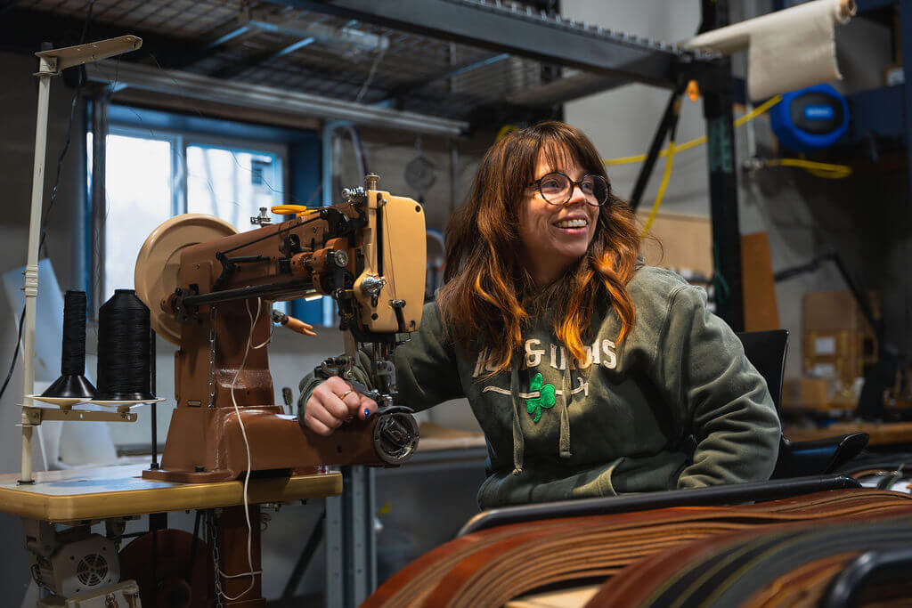 Courtney owner of axe and awl leatherworks sits in front of the sewing machine in the leather workshop smiling.