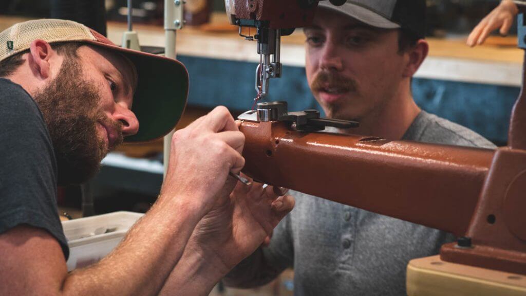 spencer and travis of axe and awl leatherworks craft leather goods on a sewing machine in the leather workshop in waynesville, nc