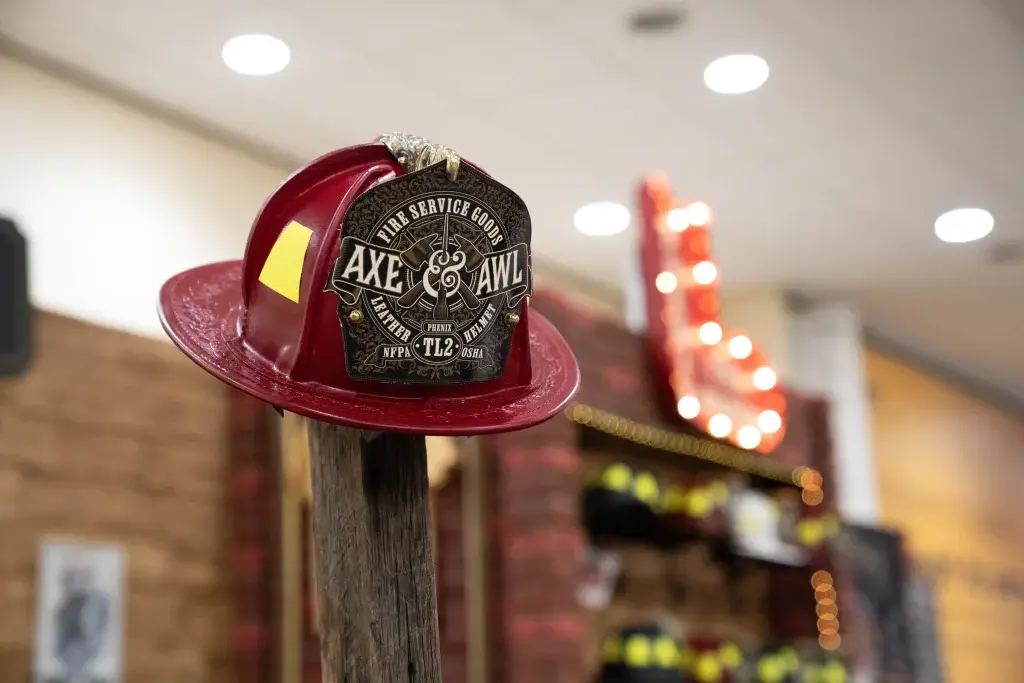 a scarlet red phenix tl-2 fireservice helmet hanging up at the fdic trade show with axe and awl leatherworks