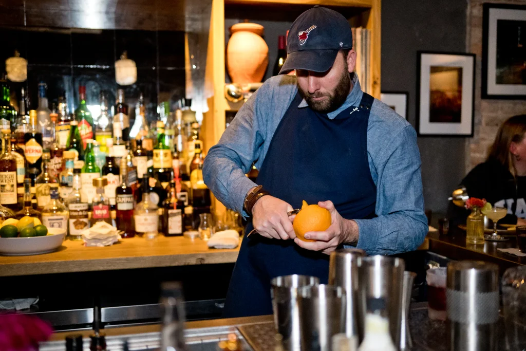 spencer tetrault peeling an orange for a fresh cockail inside bevel bar in downtown waynesville