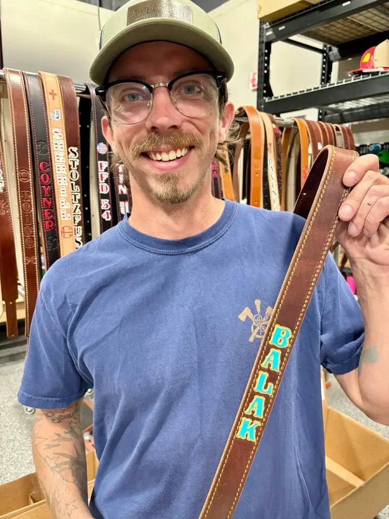 travis holds up a walnut radio strap with a blue fill and gold outline