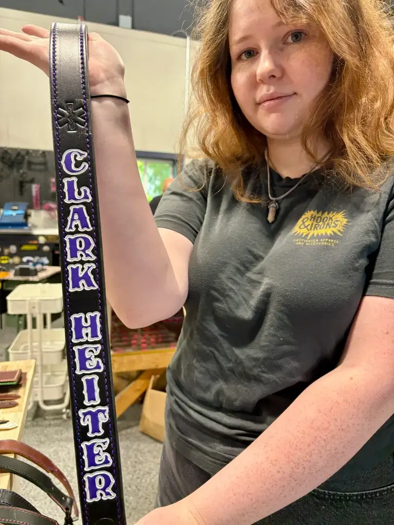 Lizzie holds up a black radio strap with purple fill and white outline