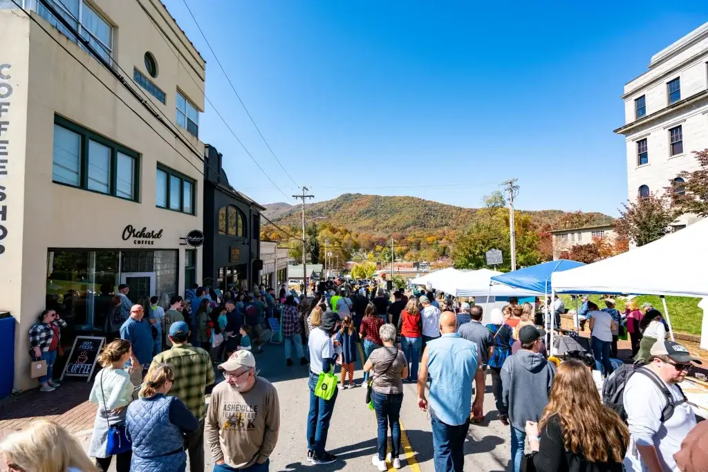 An image of vendors and a lot of people on Depot St. looking towards the band and mountains. 